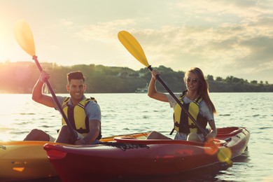 Couple in life jackets kayaking on river at sunset. Summer activity