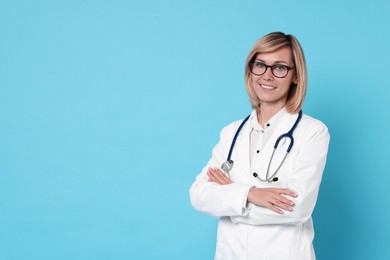 Photo of Smiling doctor with crossed arms on light blue background. Space for text