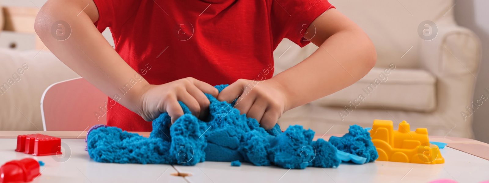Image of Little boy playing with bright kinetic sand at table indoors, closeup. Banner design