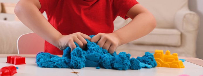 Image of Little boy playing with bright kinetic sand at table indoors, closeup. Banner design