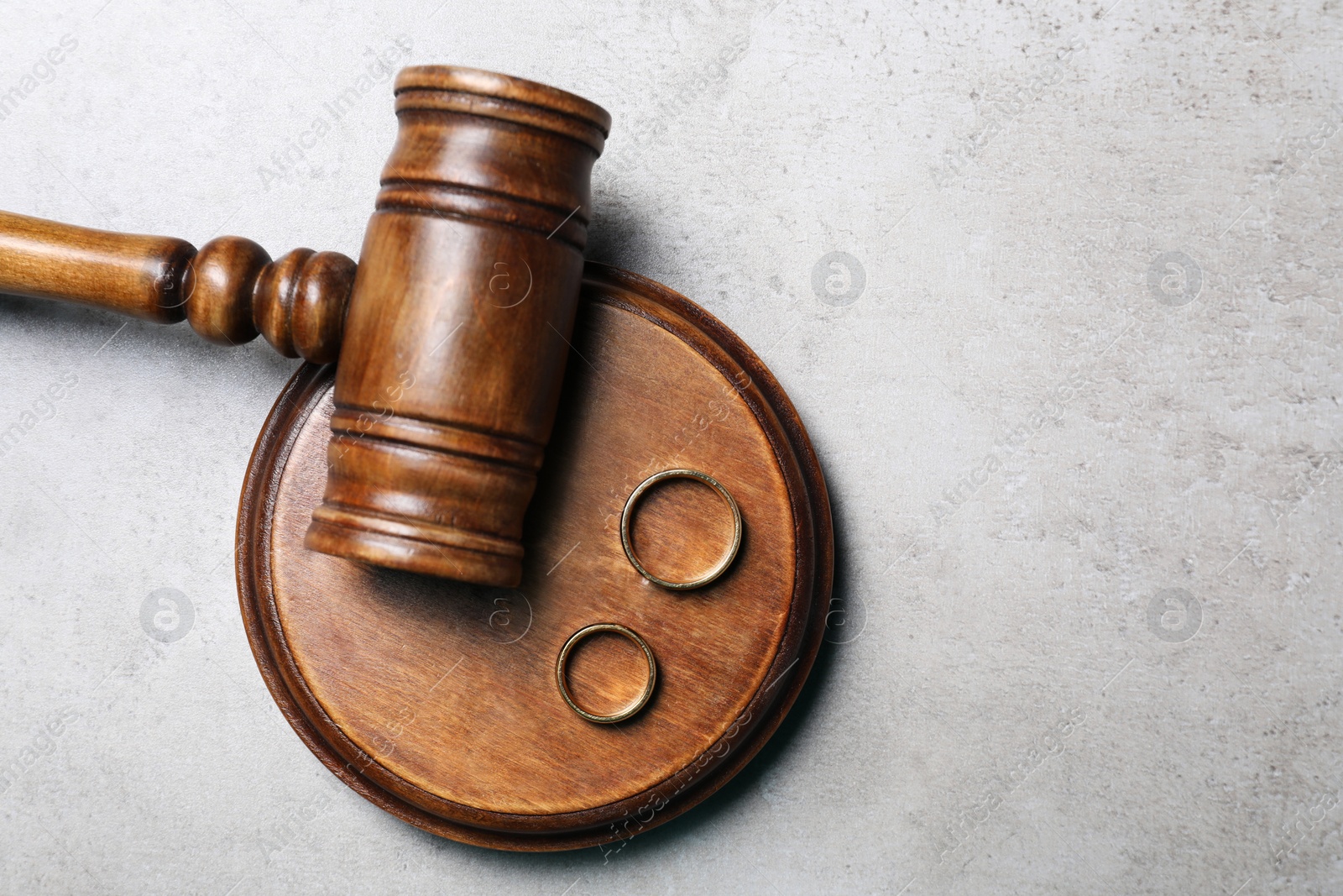 Photo of Divorce concept. Wooden gavel and wedding rings on grey table, top view with space for text