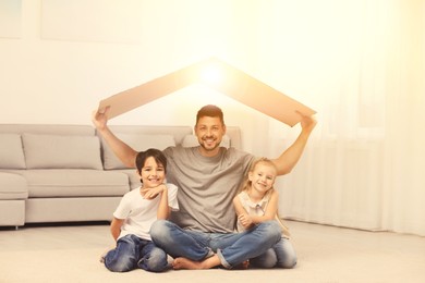 Image of Happy father and his children sitting under cardboard roof at home. Insurance concept