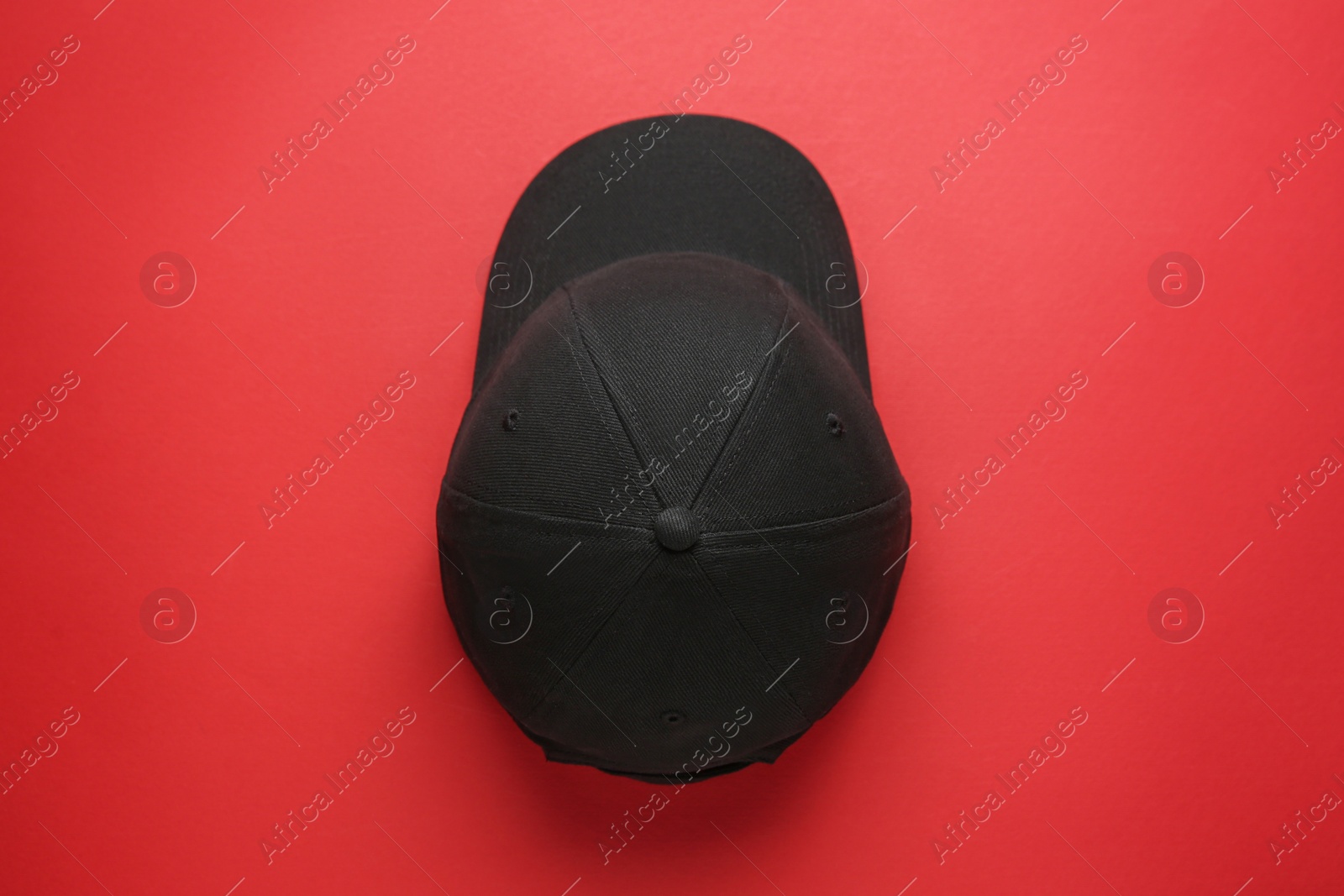 Photo of Stylish black baseball cap on red background, top view