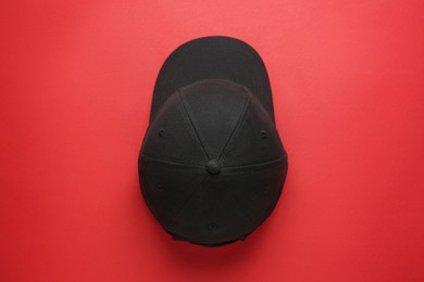 Photo of Stylish black baseball cap on red background, top view