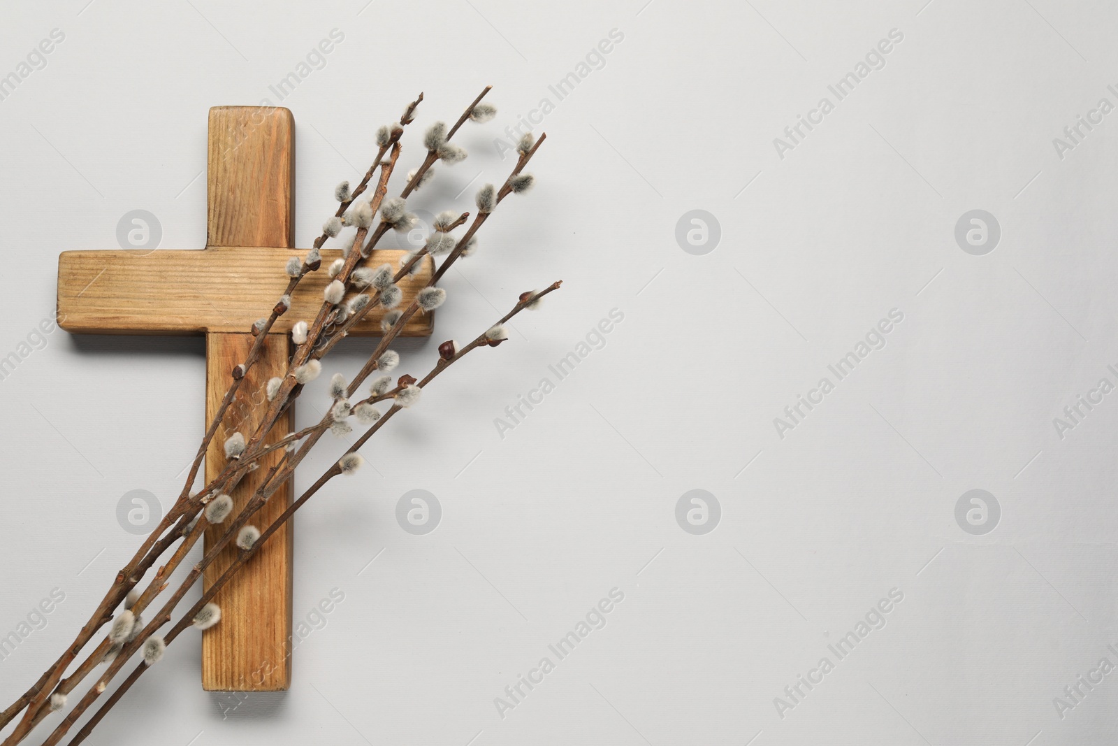 Photo of Wooden cross and willow branches on light grey background, top view with space for text. Easter attributes