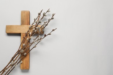 Photo of Wooden cross and willow branches on light grey background, top view with space for text. Easter attributes