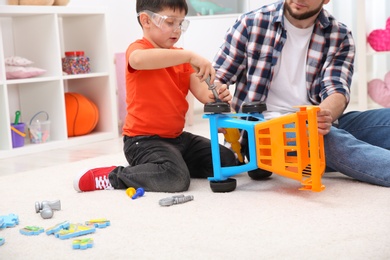 Man and his child as repairman playing with toy cart at home