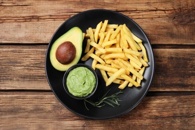 Photo of Plate with french fries, guacamole dip and avocado served on wooden table, top view