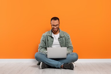 Photo of Smiling young man working with laptop near orange wall