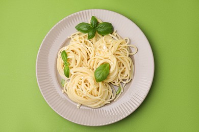 Delicious pasta with brie cheese and basil leaves on light green background, top view