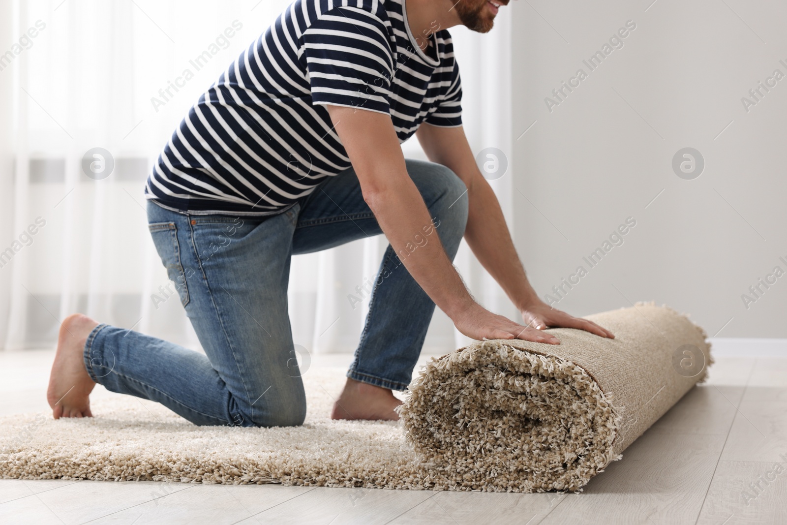 Photo of Man unrolling carpet on floor in room, closeup