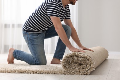 Photo of Man unrolling carpet on floor in room, closeup