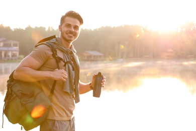 Young man drinking water on shore of beautiful lake. Camping season