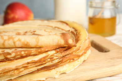 Stack of fresh thin pancakes on wooden board, closeup