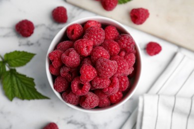 Photo of Bowl with fresh ripe raspberries on white marble table, flat lay