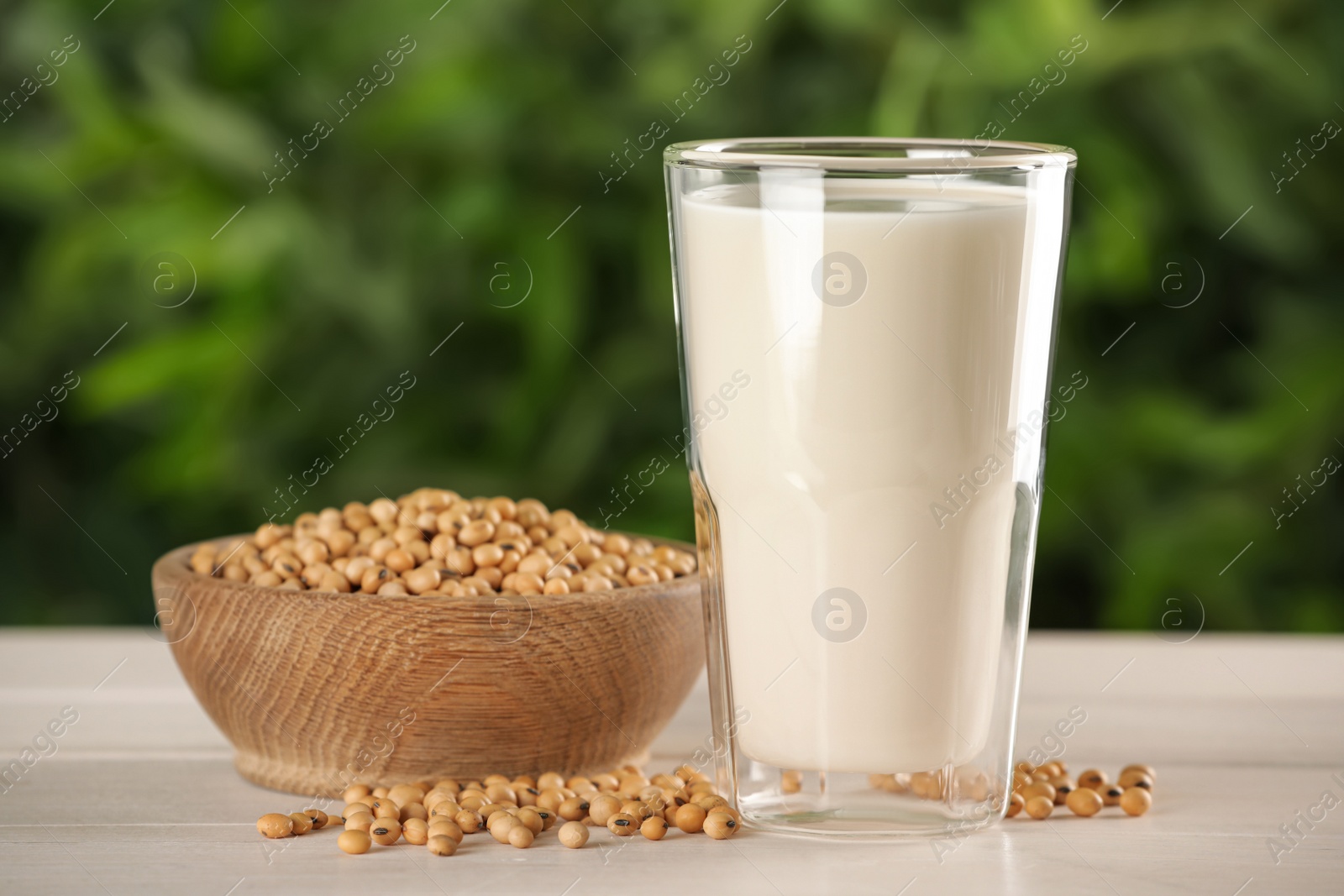 Photo of Glass with fresh soy milk and grains on white wooden table against blurred background