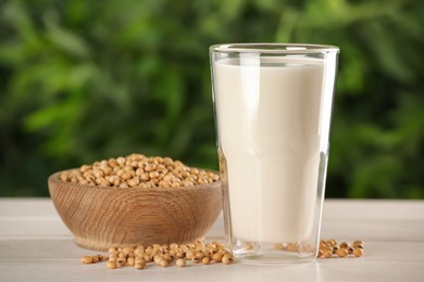 Glass with fresh soy milk and grains on white wooden table against blurred background