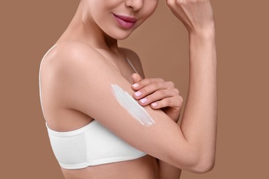 Photo of Woman with smear of body cream on her arm against light brown background, closeup