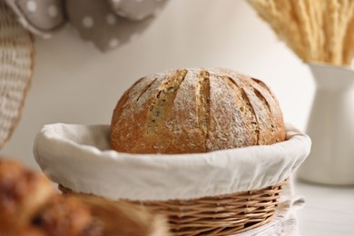 Photo of Wicker bread basket with freshly baked loaf on white marble table in kitchen, closeup