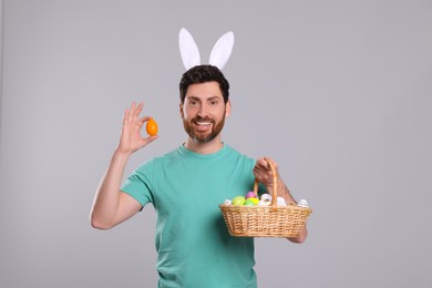 Photo of Portrait of happy man in cute bunny ears headband holding Easter eggs on light grey background
