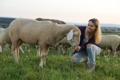 Photo of Smiling woman feeding cute sheep on pasture. Farm animals