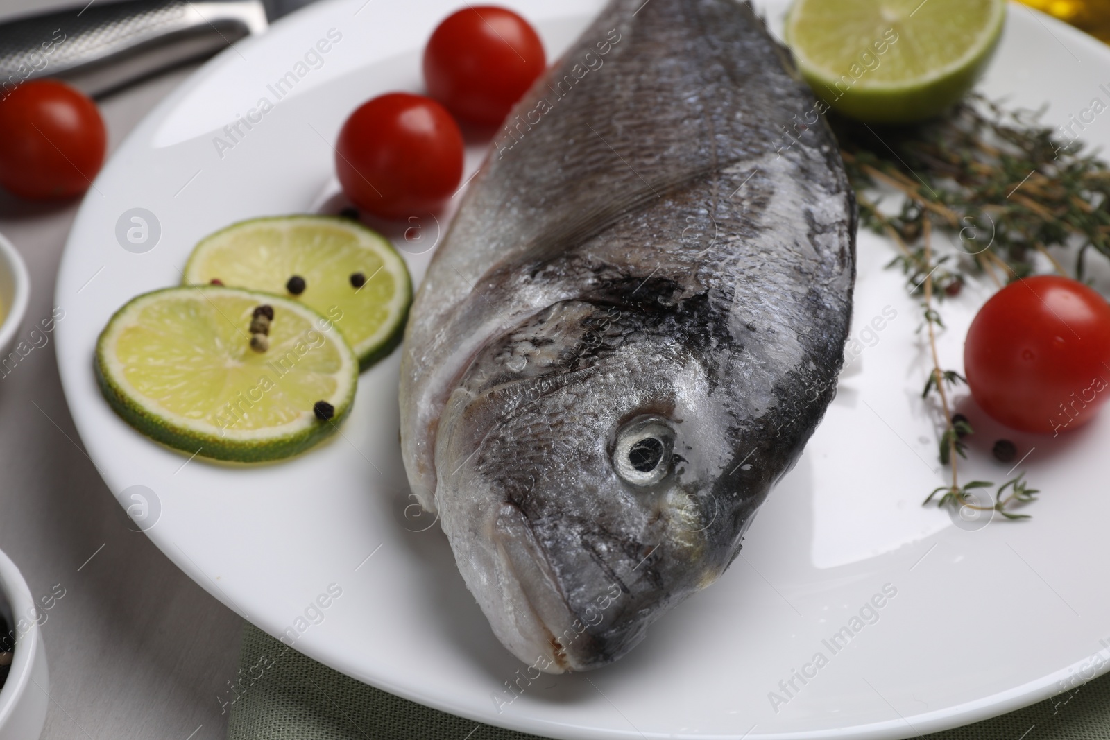 Photo of Raw dorado fish, lime slices, tomatoes and thyme on table, closeup