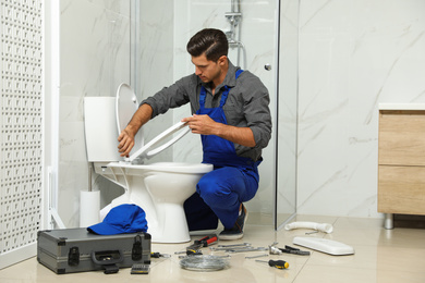 Professional plumber working with toilet bowl in bathroom