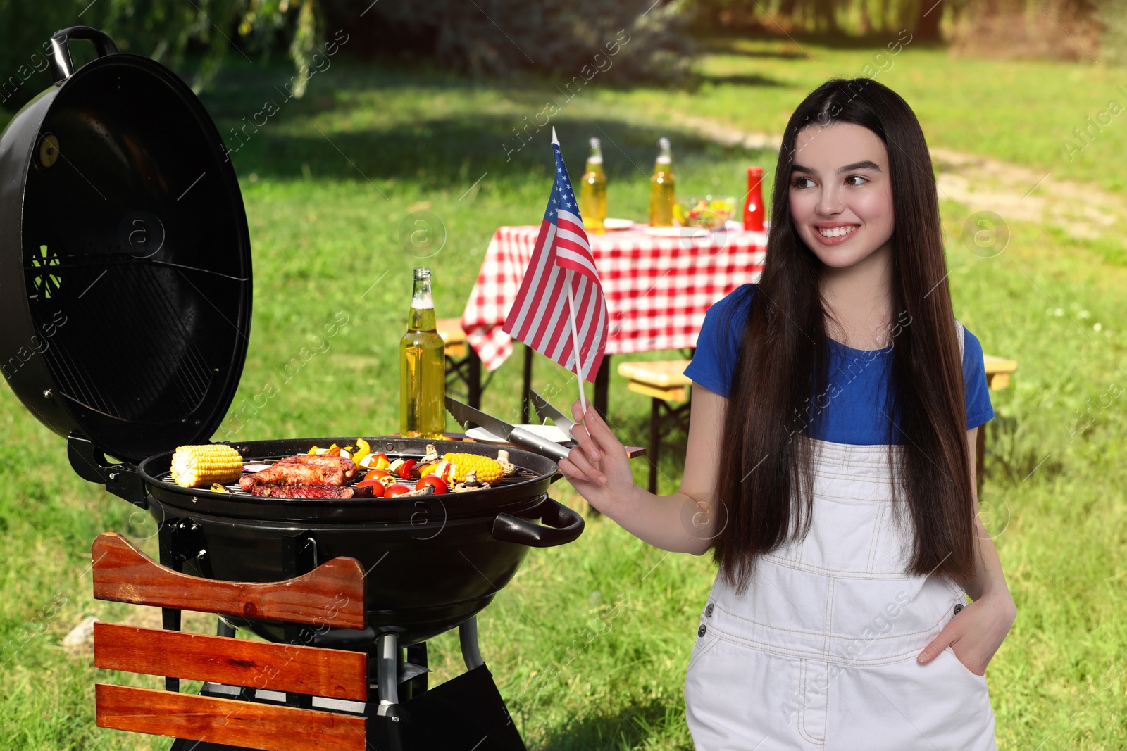 Image of 4th of July - Independence day of America. Happy girl with national flag of United States having picnic in park