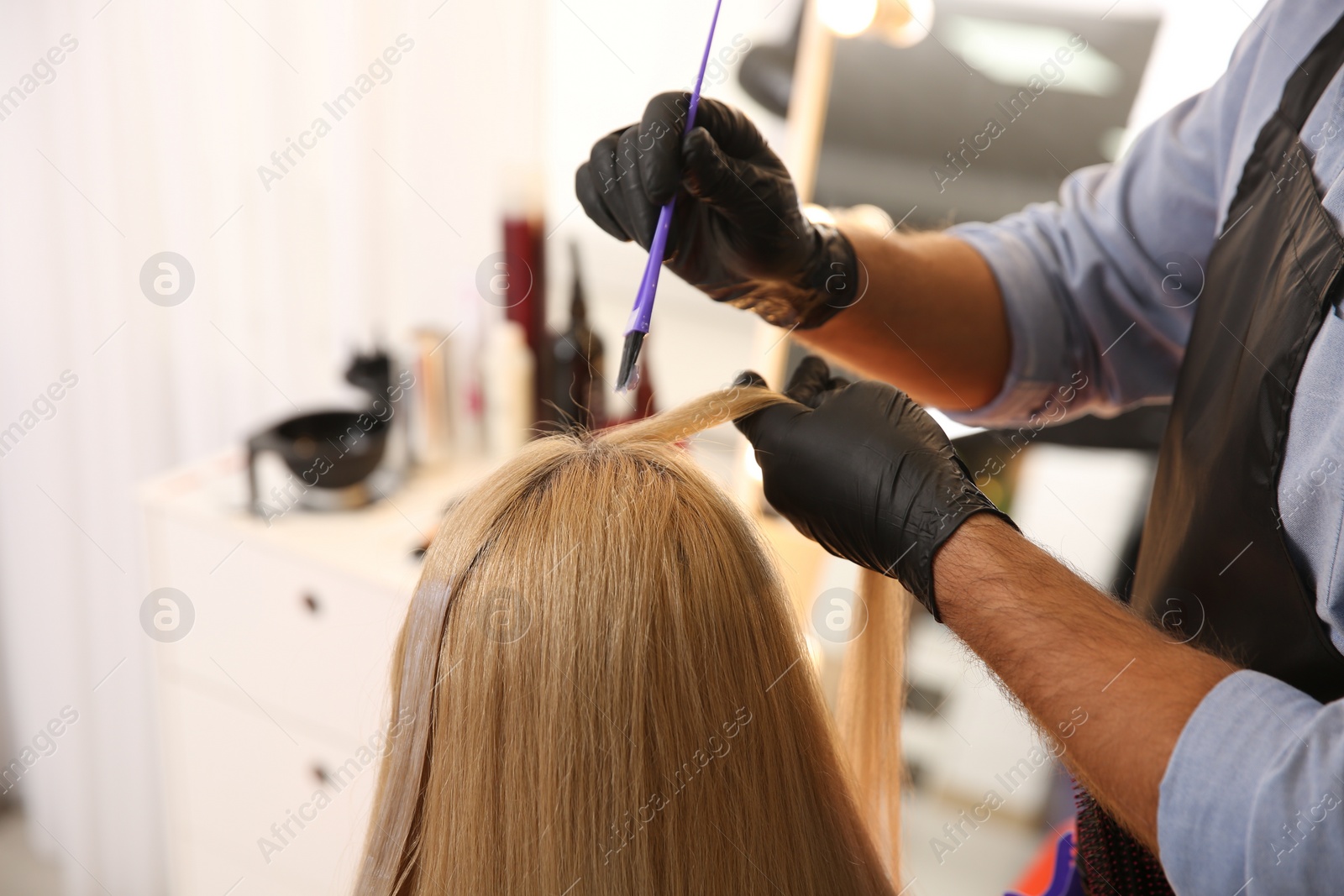 Photo of Professional hairdresser dying hair in beauty salon, closeup