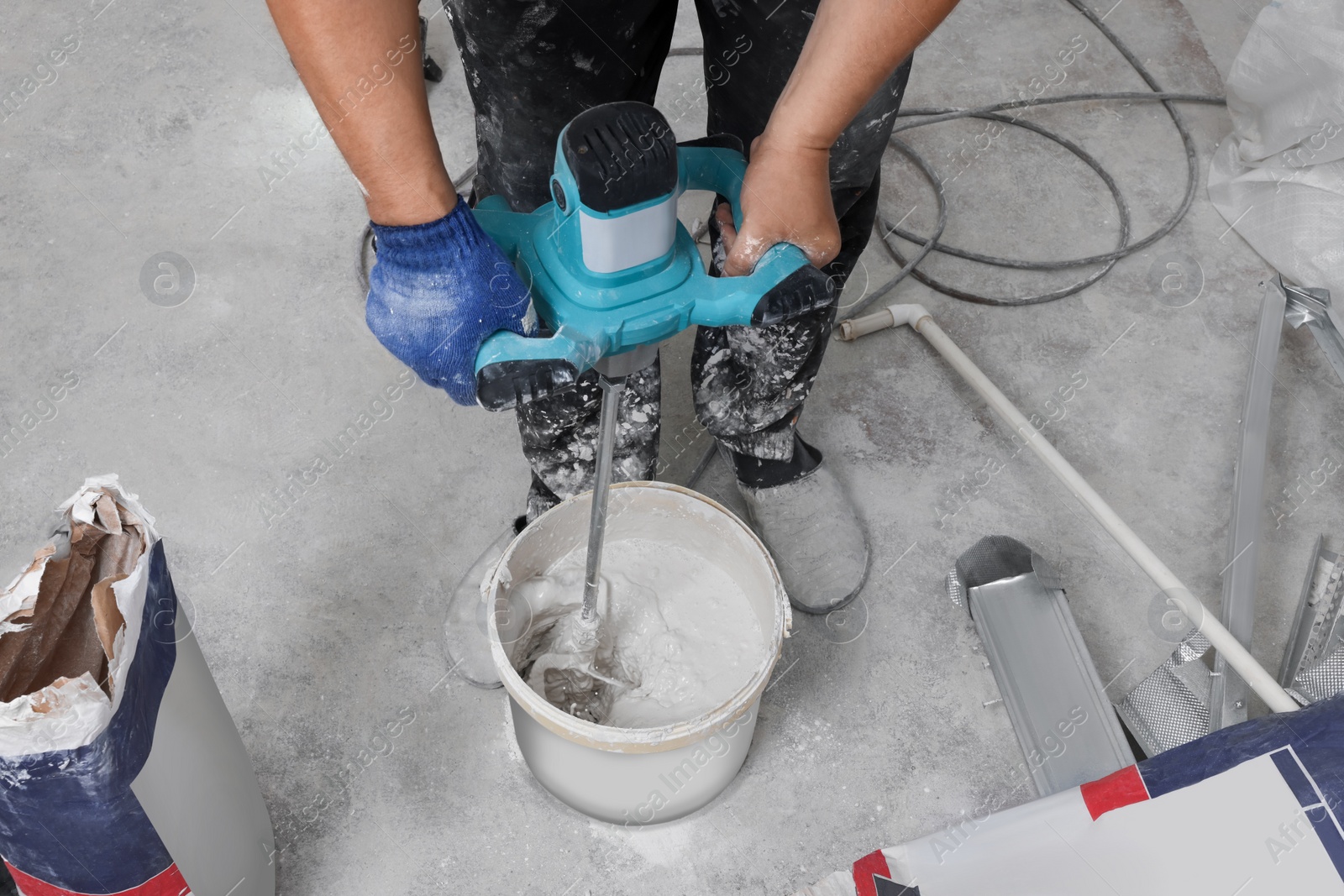 Photo of Professional worker mixing plaster in bucket indoors, closeup