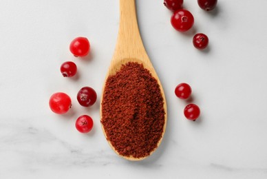 Photo of Dried cranberry powder in spoon and fresh berries on white marble table, top view