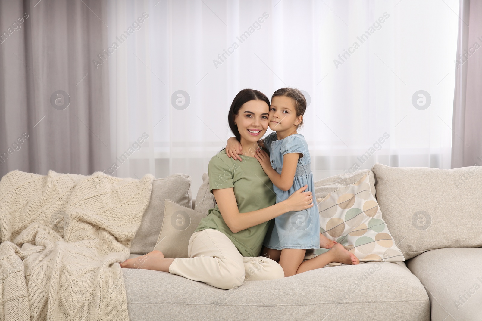 Photo of Happy woman and her cute daughter spending time together on sofa at home. Mother's day celebration