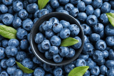 Tasty fresh blueberries with green leaves and bowl, top view