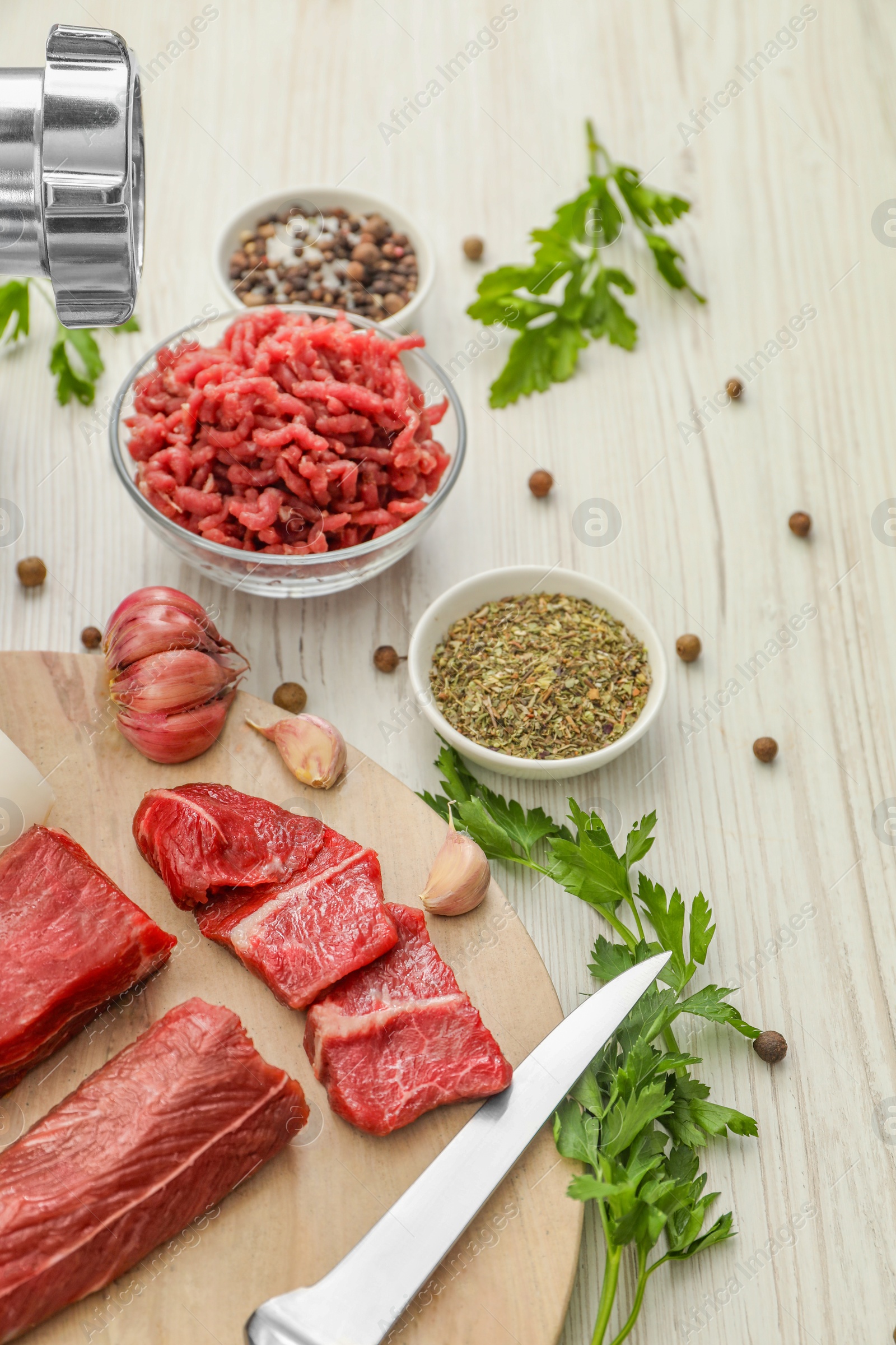 Photo of Meat grinder, beef, garlic, parsley and spices on white wooden table