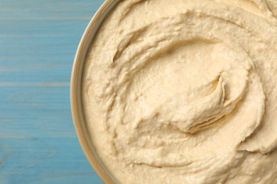 Photo of Top view of tasty hummus in bowl on light blue wooden table, closeup