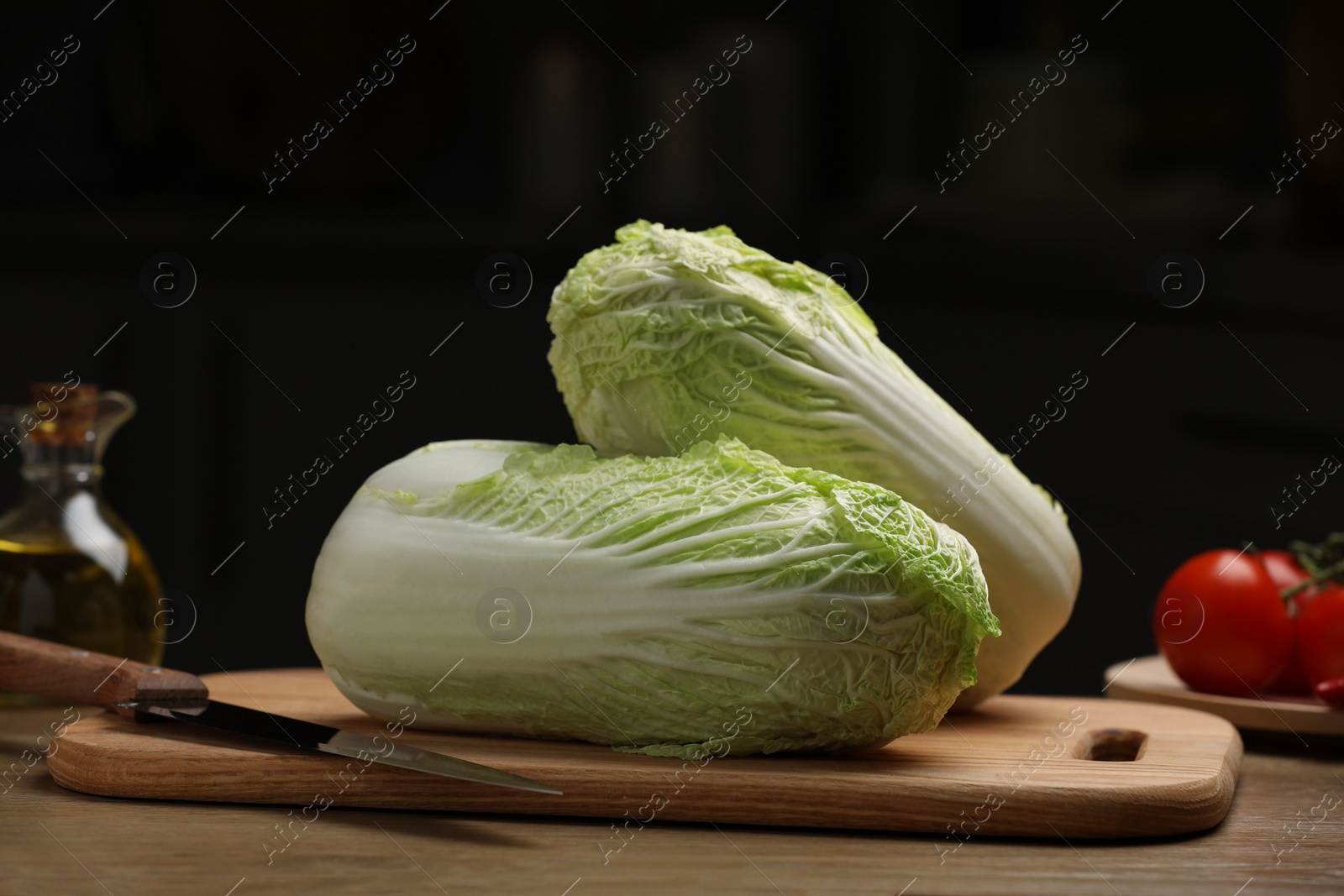 Photo of Fresh Chinese cabbages, knife, tomatoes and oil on wooden table