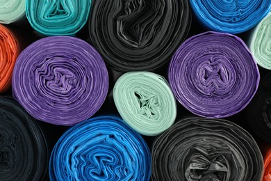 Rolls of different color garbage bags as background, top view