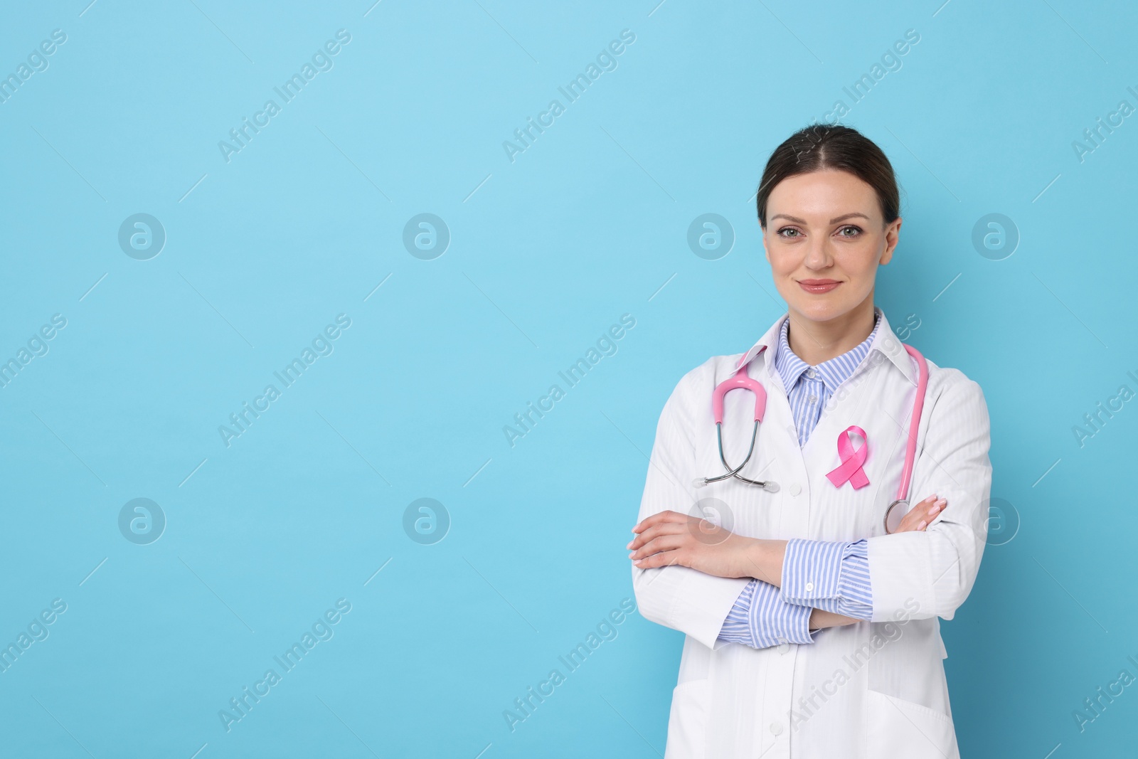 Photo of Mammologist with pink ribbon on light blue background, space for text. Breast cancer awareness