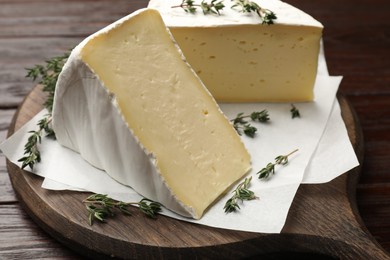 Photo of Pieces of tasty camembert cheese and thyme on wooden table, closeup