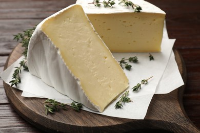 Pieces of tasty camembert cheese and thyme on wooden table, closeup