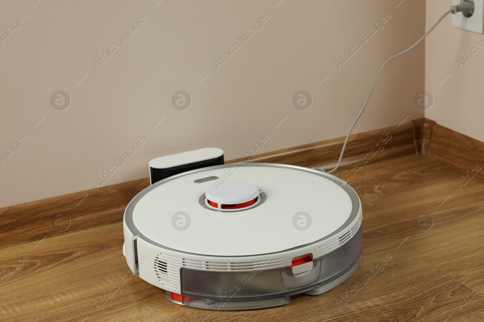 Photo of Robotic vacuum cleaner charging on wooden floor indoors