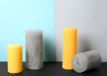 Photo of Decorative wax candles on table against color background