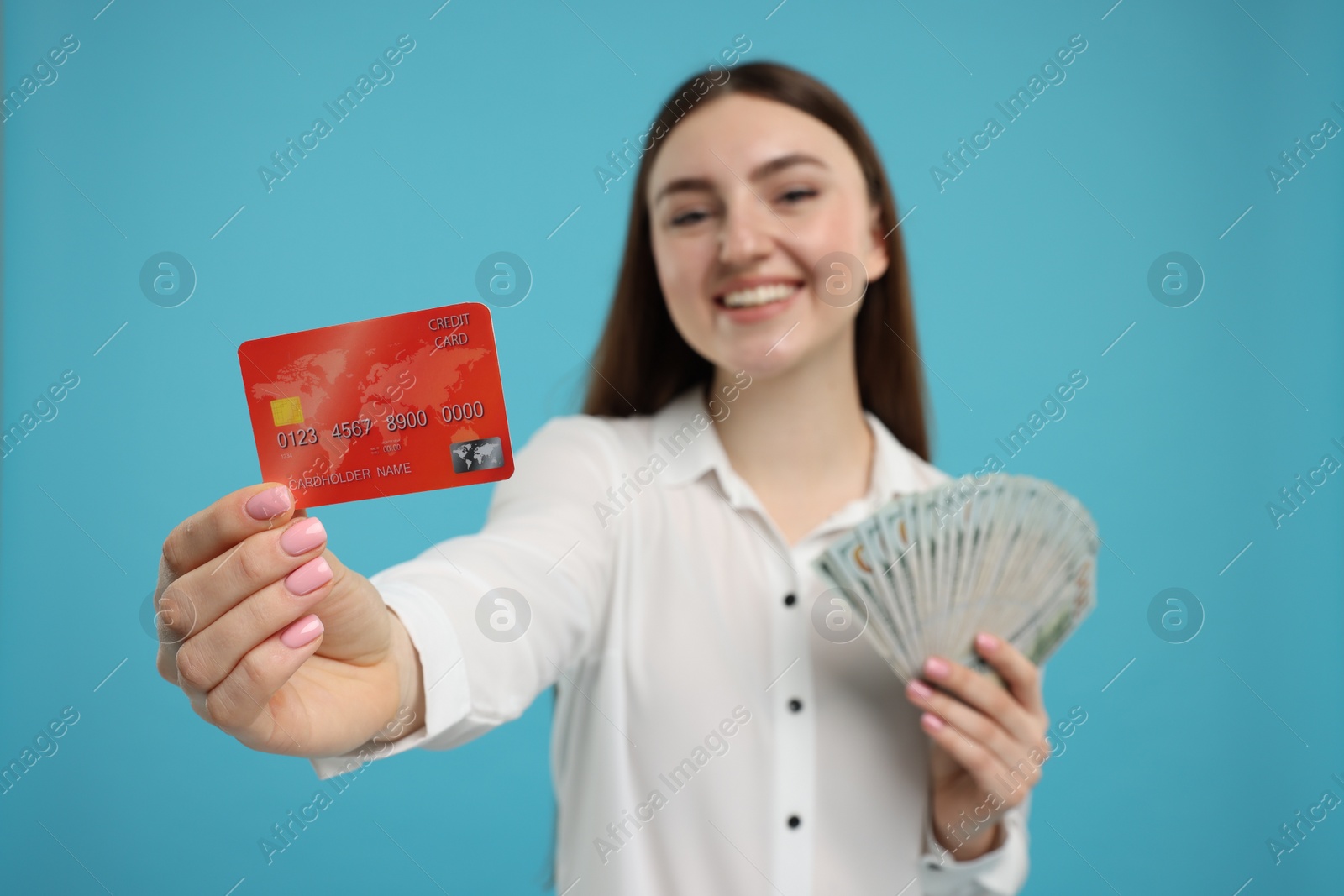 Photo of Happy woman with credit card and dollar banknotes on light blue background, selective focus