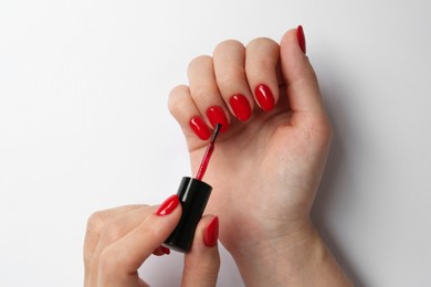 Photo of Woman painting nails with red polish on white background, closeup