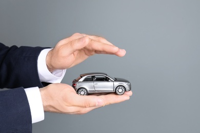 Male insurance agent holding toy car on grey background, closeup. Space for text