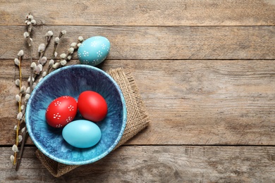 Photo of Flat lay composition of bowl with painted Easter eggs and pussy willow on wooden table, space for text