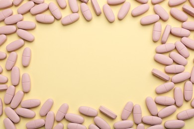 Photo of Frame made of vitamin pills on pale yellow background, top view. Space for text