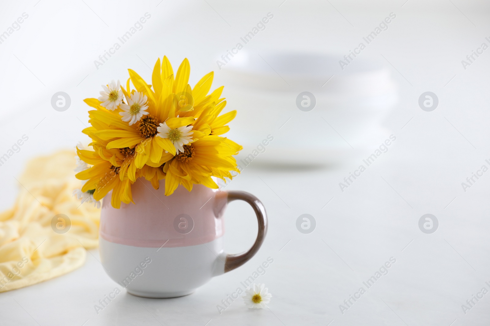 Photo of Cup with beautiful flowers on white table. Space for text