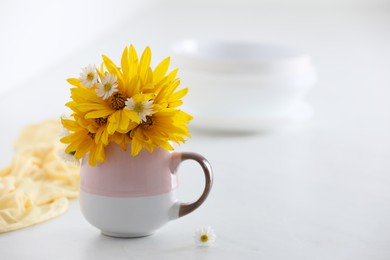 Cup with beautiful flowers on white table. Space for text