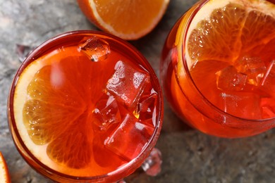 Photo of Aperol spritz cocktail, ice cubes and orange slices in glasses on grey textured table, top view